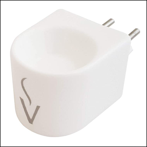 A imagem mostra um aromatizador branco de tomada. Ele tem formato ovalado, um pequeno círculo no centro da parte superior rebaixado e um desenho de um V com uma pequena fumaça em cima, na parte da frente. O fundo da imagem é branco.