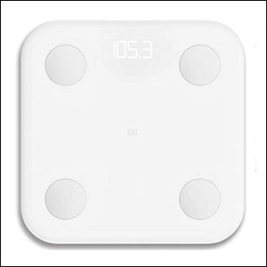 A imagem mostra uma balança branca e quadrada, com 4 círculos pequenos em cada um de seus cantos e um pequeno visor luminoso que mostra o peso. O fundo da imagem é branco.