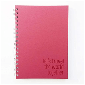 A imagem mostra um caderno retangular grande, com espiral prata. A capa é da cor rosa e, no canto inferior direito, há a frase "Let's travel the world together", também em rosa. O fundo da imagem é branco.