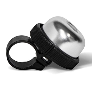 Campainha-para-Bicicleta-com-Suporte-Atrio A imagem mostra uma campainha de bicicleta redonda na cor prata com um apoio preto em sua base. O fundo da imagem é branco.