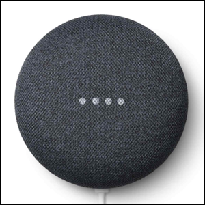 A imagem mostra o alto-falante Nest Mini, que tem um formato redondo, na cor cinza. É possível ver 4 pontos brancos em cima do alto falante, demonstrando que ele está ligado. O fundo da imagem é branco.