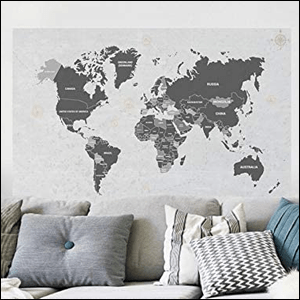 A imagem mostra um quadro adesivo em formato de mapa mundi com os países em cinza escuro, atrás de um sofá cinza com almofadas cinzas e azuis.