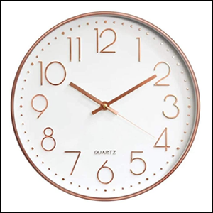 A imagem mostra um relógio de parede redondo, com moldura rose gold. O fundo do relógio é branco e os números e ponteiros também são rose gold. O fundo da imagem é branco.