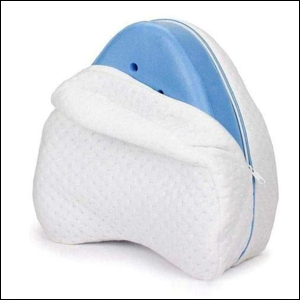 A imagem mostra um travesseira que possui formato de coração invertido. O travesseiro possui uma capa branca que está levemente aberta, mostrando o enchimento na cor azul do travesseiro, que possui também alguns furos para ventilação. O fundo da imagem é branco.
