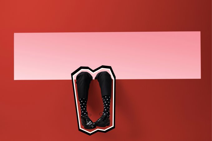 A imagem apresenta um fundo vermelho, com uma faixa rosa da onde é possível ver duas pernas saindo, como se alguém estivesse pendurando-as. A pessoa que pendura as pernas está usando uma calça curta e é possível ver as meias de bolinha que esta usando junto com os sapatos, também pretos.