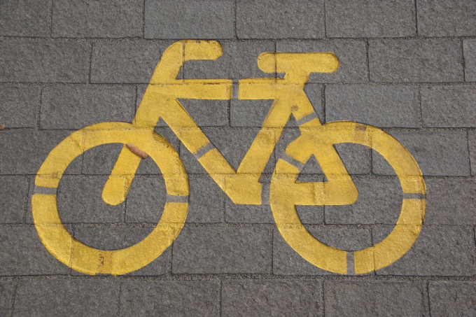 A imagem mostra um chão com ladrilhos cinzas onde há o desenho de uma bicicleta pintado em amarelo.