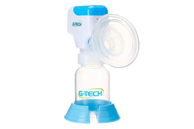 A imagem mostra uma bomba de tirar leite, feita de plástico, com uma concha de silicone para encaixe no seio e um recipiente transparente para o armazenamento do leite, que fica apoiado sobre uma base azul claro. O fundo da imagem é branco.