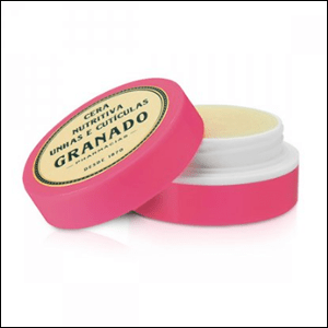 Cera-Nutritiva-de-Cutícula-Granado-Pink A imagem mostra um recipiente redondo, na cor rosa, aberto, mostrando uma cera na cor creme. A tampa da embalagem está apoiada no recipiente, também na cor rosa e com o logo da Granado em cima: um círculo amarelado com as letras em verde escuro.