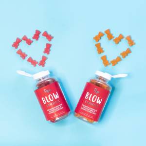 blow-gummies A imagem mostra dois frascos do produto Blow Gummies, feitos de plástico, com rótulo rosa e o nome do produto escrito. As tampas brancas estão abertas e, em cima de cada uma, há um coração formado pelas gummies, o produto dentro do frasco. O fundo da imagem é azul.
