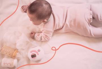 A imagem mostra um bebê deitado de bruços em uma cama, com várias bombinhas de leite ao seu lado.