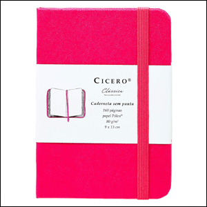 A imagem mostra uma caderneta retangular, na cor rosa pink, com um elástico na mesma cor, colocado na vertical, e uma faixa branca no centro do caderno, contento suas informações e o nome da marca do caderno.