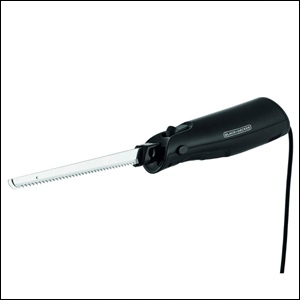 Faca-Elétrica-220V-Black+Decker A imagem mostra uma faca de serra, feita de aço inox, presa a uma base na cor preta, com formato ergonômico para ser possível segurá-la. Na base, é possível ver um fio preto conectado a ela, que liga a face elétrica na tomada. O fundo da imagem é branco.