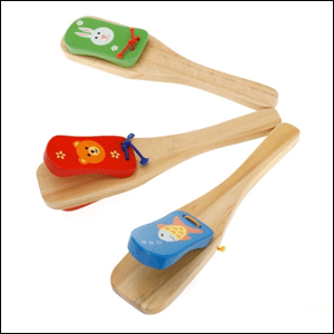 A imagem mostra um instrumento de madeira, composto por 3 alças de madeira, com pequenas peças coloridas, também de madeira, amarradas na ponta, formando uma espécie de castanhola.