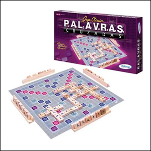 A imagem mostra o tabuleiro do jogo aberto, com vários quadrados e, em seus 4 lados, peças de apoio que seguram pequenas peças quadradas com letras em cada uma delas. Atrás do tabuleiro, é possível ver a caixa do jogo em pé. O fundo da imagem é branco.