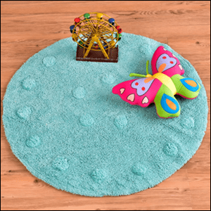 Tapete-Infantil-de-Algodão-Verde-Etna A imagem mostra um tapete de algodão redondo, na cor azul, com pequenas bolinhas na mesma cor do tapete nas bordas e no centro. Ele está sobre um piso de madeira e, sobre ele, há uma roda-gigante de madeira de brinquedo e uma borboleta de pelúcia.