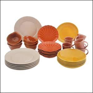 A imagem mostra um jogo de louças com pratos redondos nas cores creme e amarelo, pratos de sobremesa em formato de concha na cor laranja, xícaras na cor rosa claro e um conjunto de pequenos bowls na cor marrom.