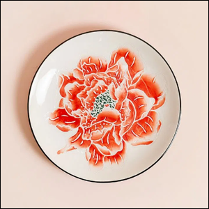 A imagem mostra um prato branco com uma flor laranja pintada ao centro.
