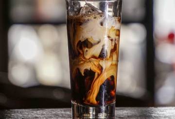 A imagem mostra um copo alto de vidro com a bebida Iced Latte dentro.