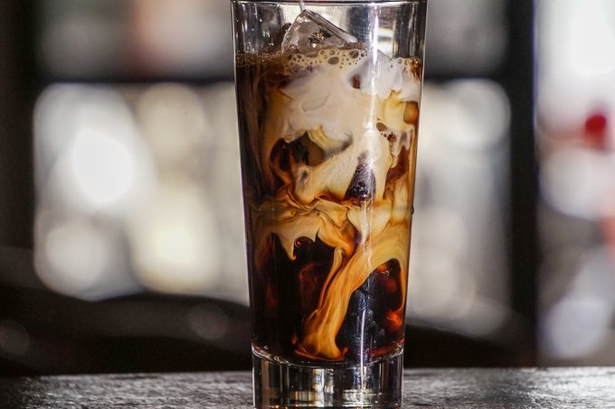 A imagem mostra um copo alto de vidro com a bebida Iced Latte dentro.