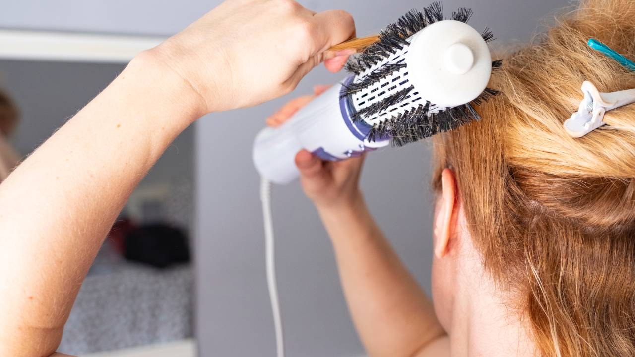 A imagem mostra uma mulher loira arrumando o cabelo com uma escova rotativa.