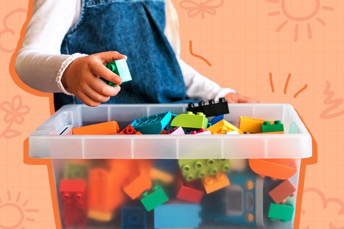 A imagem mostra uma mão de crianças guardando brinquedos numa caixa transparente.