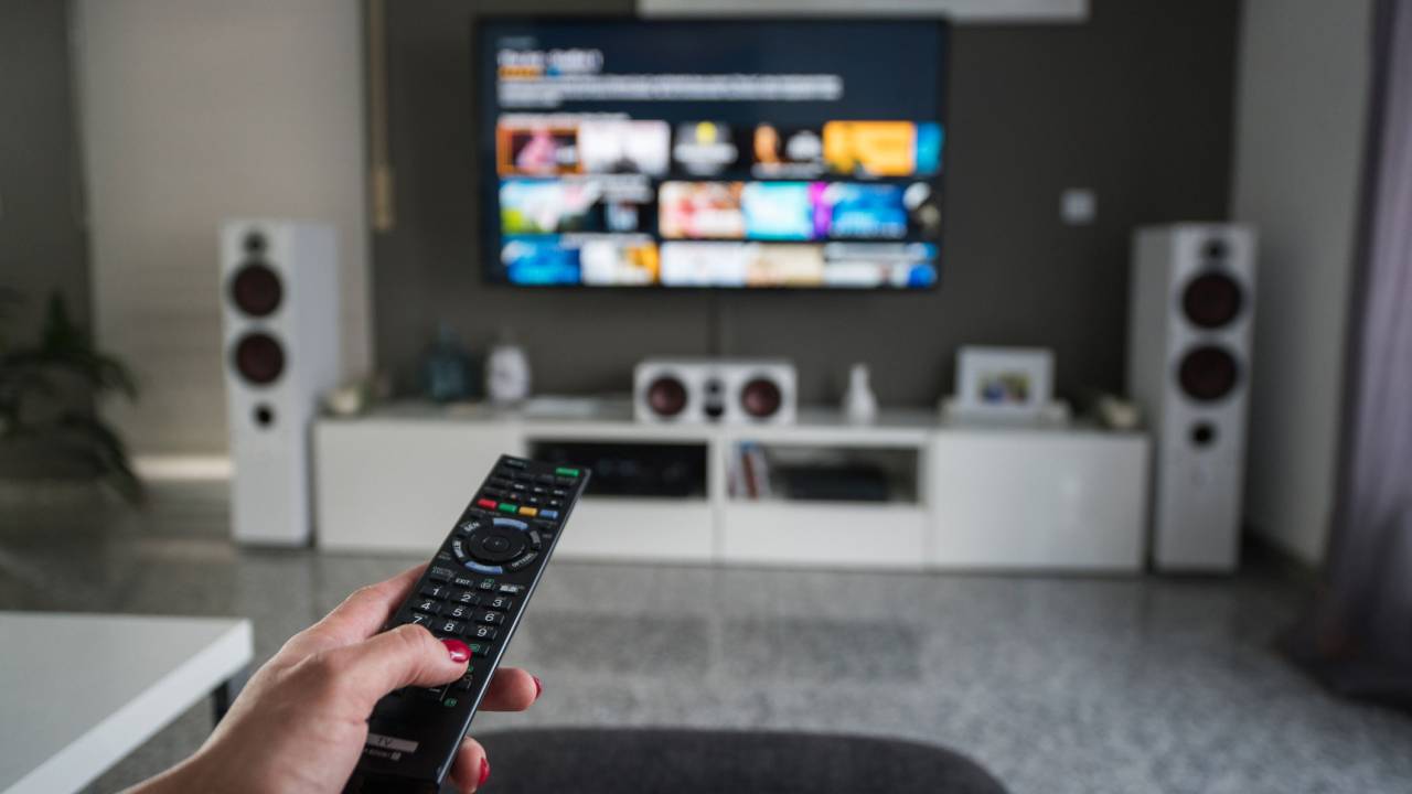 A imagem mostra uma pessoa apontando o controle remoto para uma tv ligada.