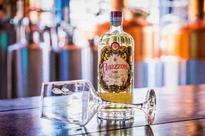 A imagem mostra uma garrafa do novo gin da Amázzoni sobre um balcão com uma taça de vidro deitada em sua frente.