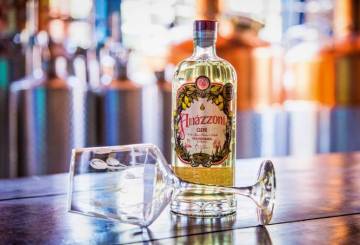 A imagem mostra uma garrafa do novo gin da Amázzoni sobre um balcão com uma taça de vidro deitada em sua frente.