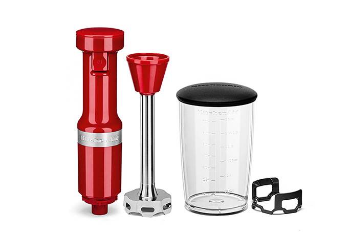 A imagem mostra um mixer, com o corpo vermelho, ao lado de um copo de acrílico e um protetor removível.