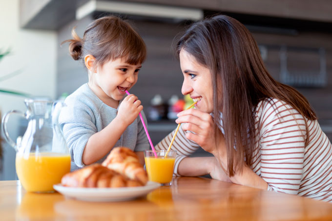 Mãe e filha na cozinha, tomando juntas suco de laranja