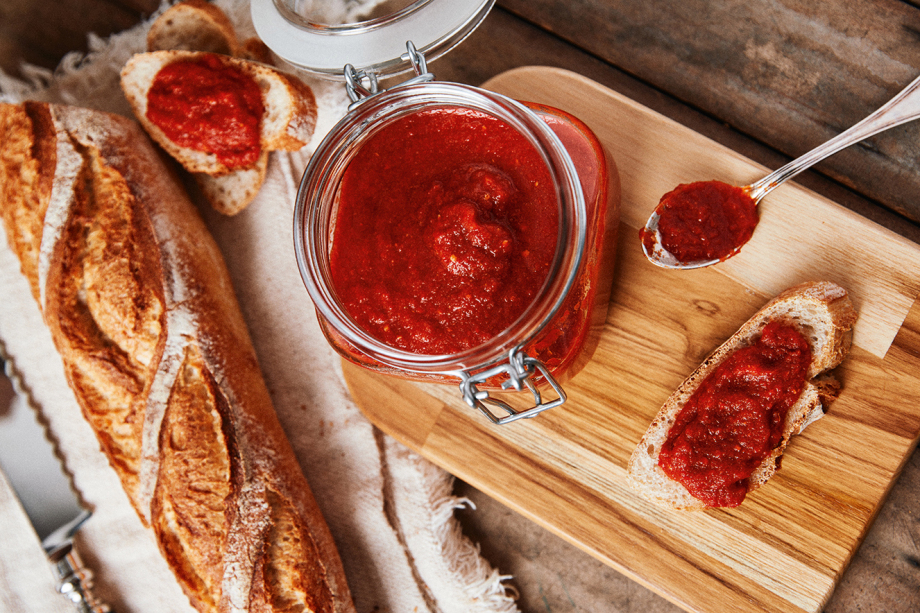Pote de pimenta com abacaxi, um pão italiano ao lado, com uma fatia cortada com a pasta de pimenta