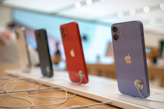 Celulares iPhone 12 alinhados, em pé, sobre bancada: cinza, vermelho, preto, bege