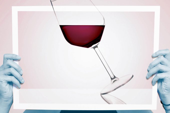 Copo de vinho tinto erguido por mãos com luvas azuis