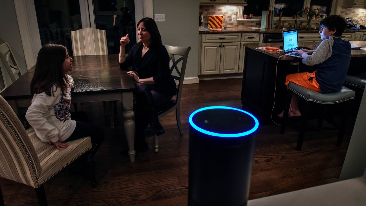 Mãe, filha e filho numa sala, à noite, com o dispositivo Alexa em primeiro plano