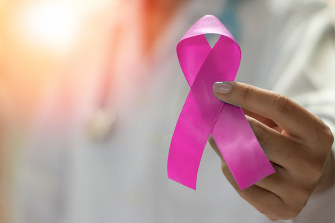 Mão feminina mostrando o laço símbolo do Outubro Rosa