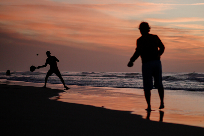 Pessoas jogando beach tennis em uma praia com pôr-do-sol