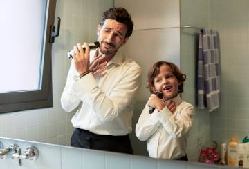 pai e filho usam barbeador elétrico em frente ao espelho