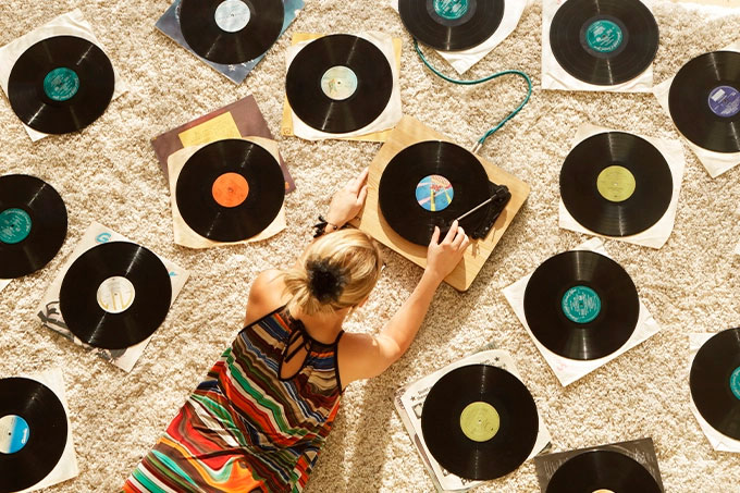 Mulher com toca-discos e vários discos de vinil sobre a areia da praia