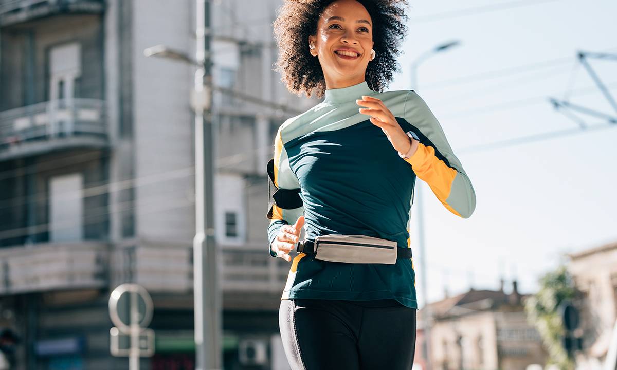 Mulher jovem corre pelas ruas da cidade usando relógio monitor e fones de ouvido