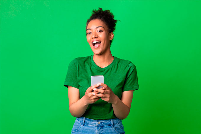 Mulher alegre com celular na mão, em frente a parede verde