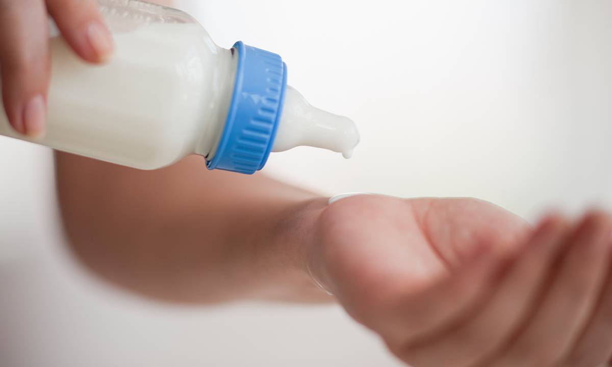 mão testando temperatura do leite da mamadeira