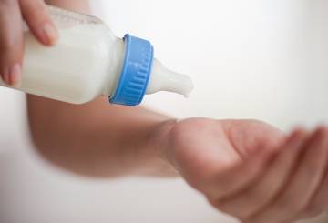 mão testando temperatura do leite da mamadeira