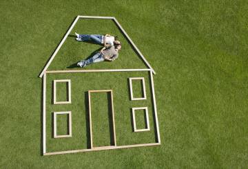 casal deitado na grama dentro de estrura de madeira que forma o desenho de uma casa