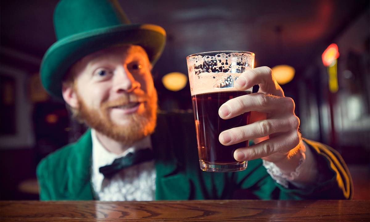 Irlandes vestido de verde e com cartola segurando uma cerveja