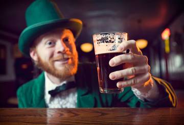 Irlandes vestido de verde e com cartola segurando uma cerveja