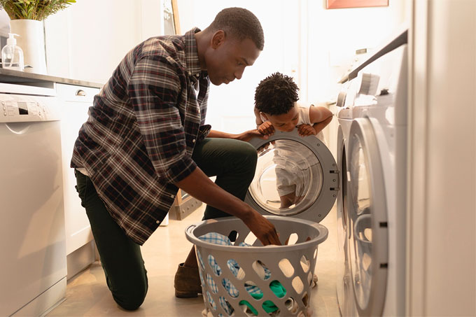 Homem e filha colocando roupa na máquina de lavar com abertura frontal