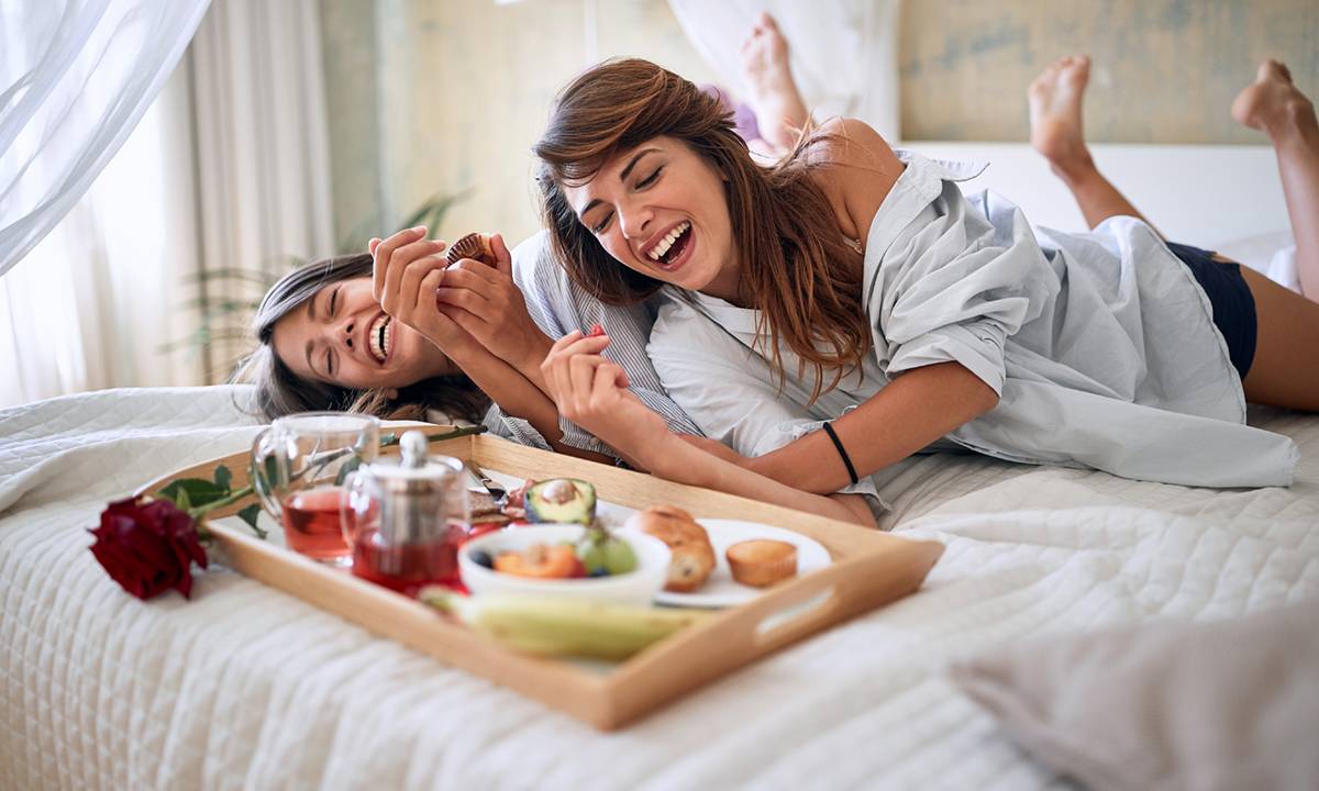 casal de mulheres na cama tomando café e rindo