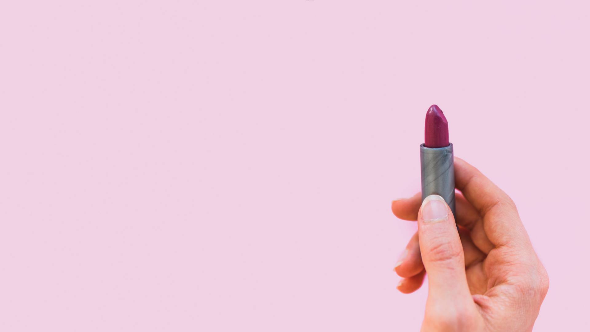 feminino-mao-segurando-o-batom-de-sombra-escura-no-fundo-rosa batom